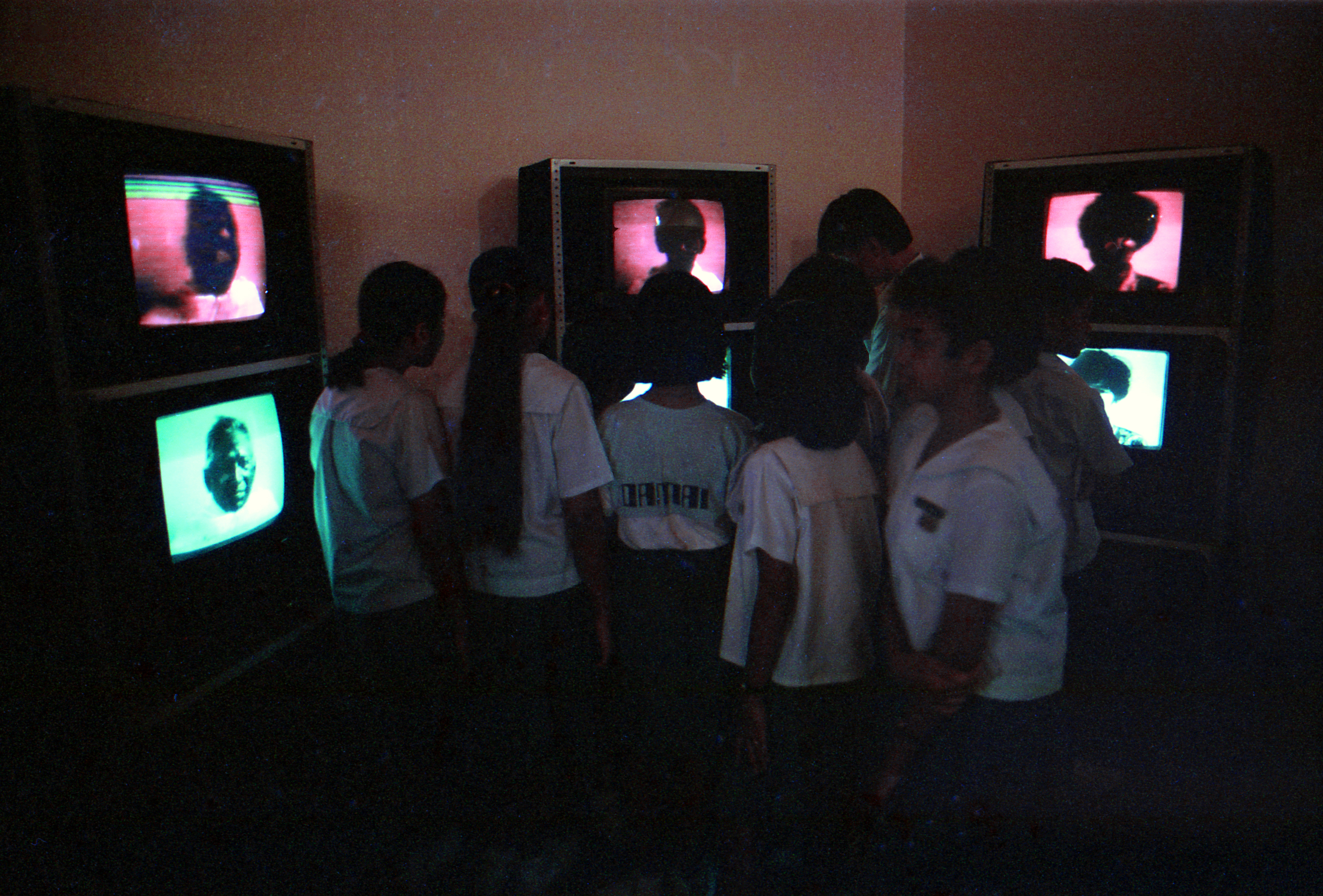 A group of primary school students gathering around three columns of televisions. Each column features a pair of televisions stacked on top of each other.